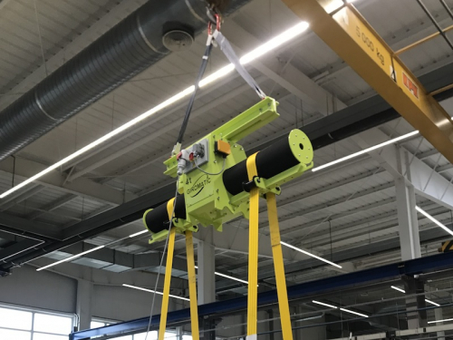 Traverza pre otáčanie bremien s nastaviteľnou roztečou kladiek<br>Otočnú časť tvorí valec s protišmykovou vrstvou, ktorá je poháňaná elektromotorom cez remenicu. Rozteč pásov je možné upraviť podľa dĺžky bremena. Pásy sú vybavené ochrannou. Traverza je ovládaná pomocou rádiového ovládania.